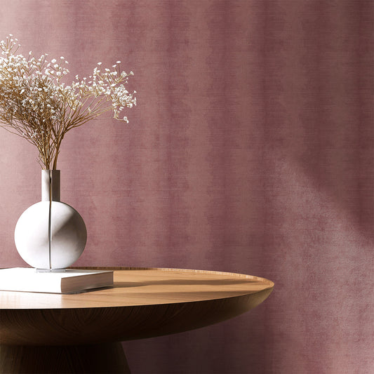 A section of wallpaper with a pink hue and a subtle lotus flower pattern, displayed in a room setting with a vase of flowers on a table.